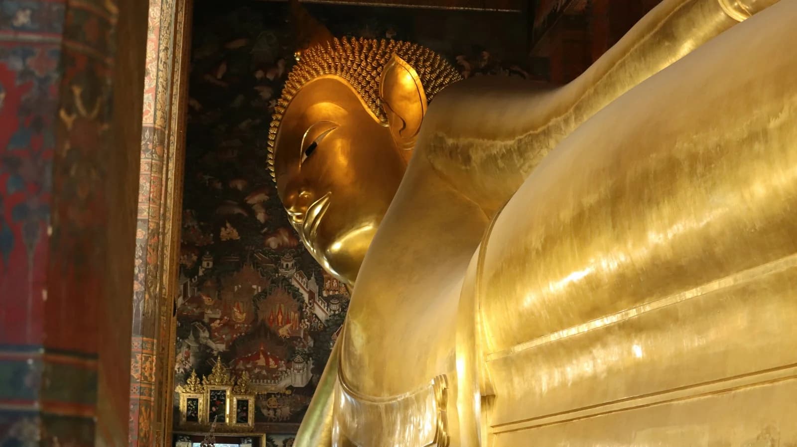 The immense golden reclining Buddha at Wat Pho, framed by painted columns and intricate temple murals.