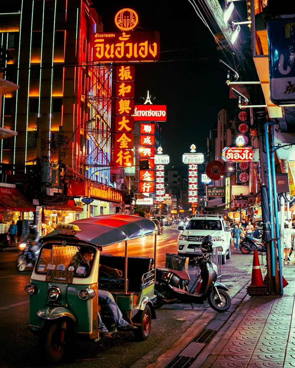 Tuk-tuks beneath glowing red and gold signs along Yaowarat Road at night.