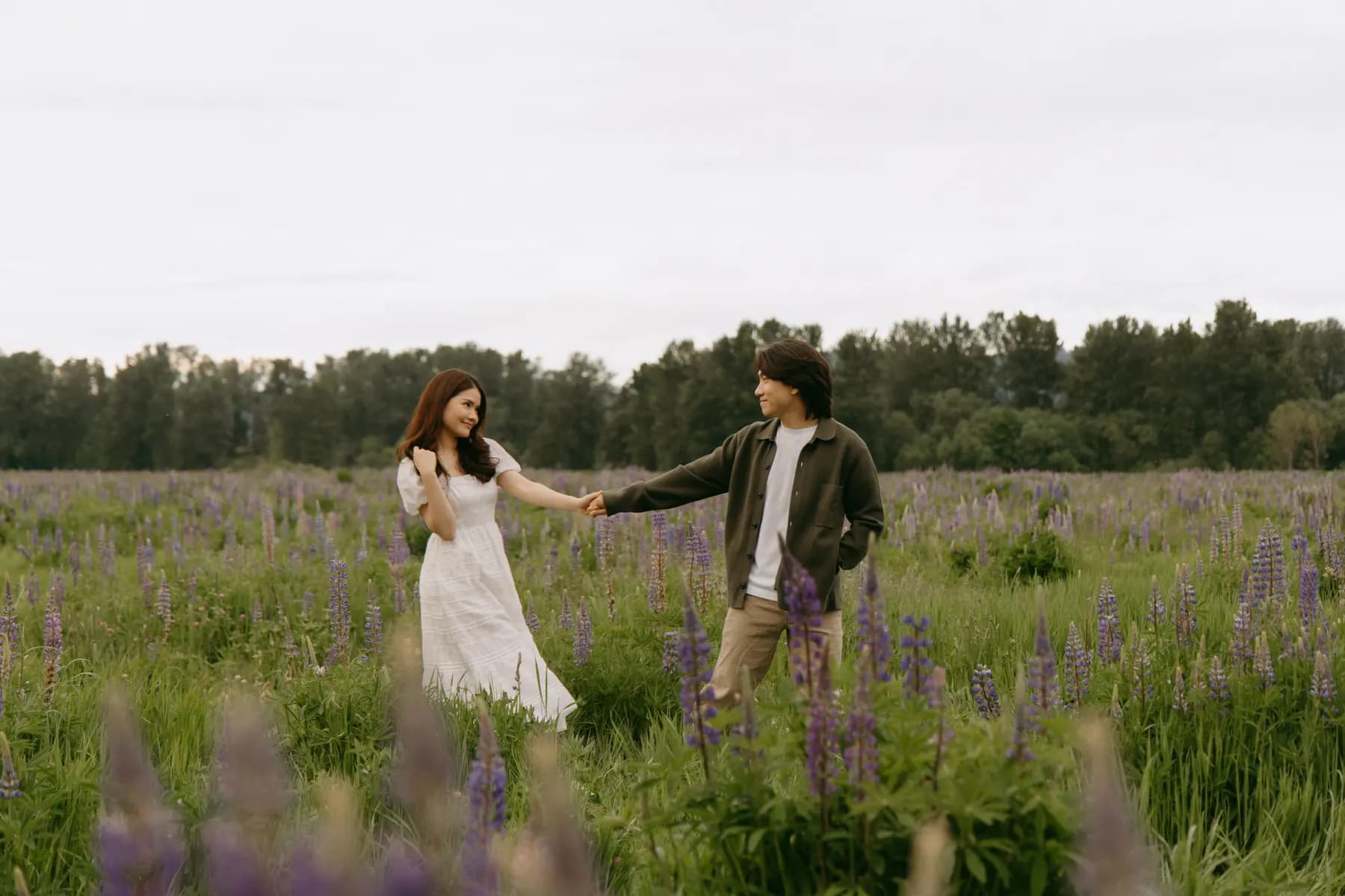 Jam leading Tony by the hand through a field of purple lupine under an overcast sky