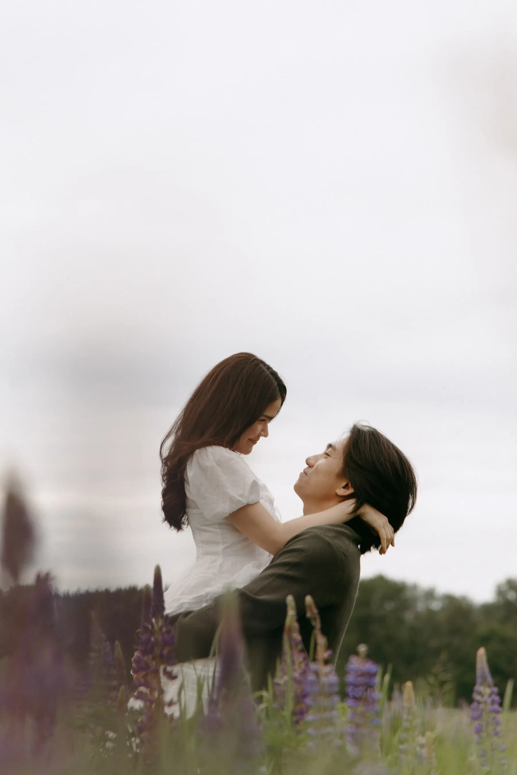 Tony lifting Jam in his arms in the lupine field, pale sky above