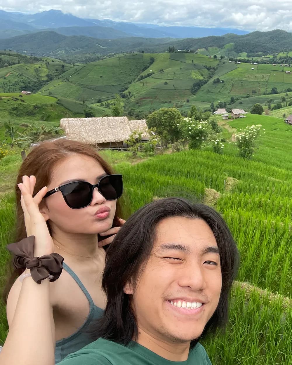 Jam and Tony in front of terraced green rice paddies and thatched huts below the mountains at Doi Inthanon