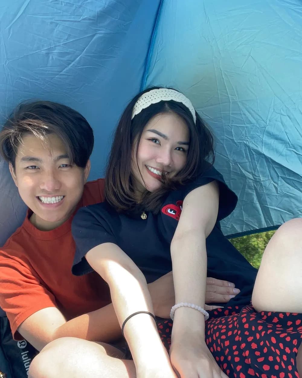 Jam and Tony sitting close together inside the blue tent, both grinning at the camera