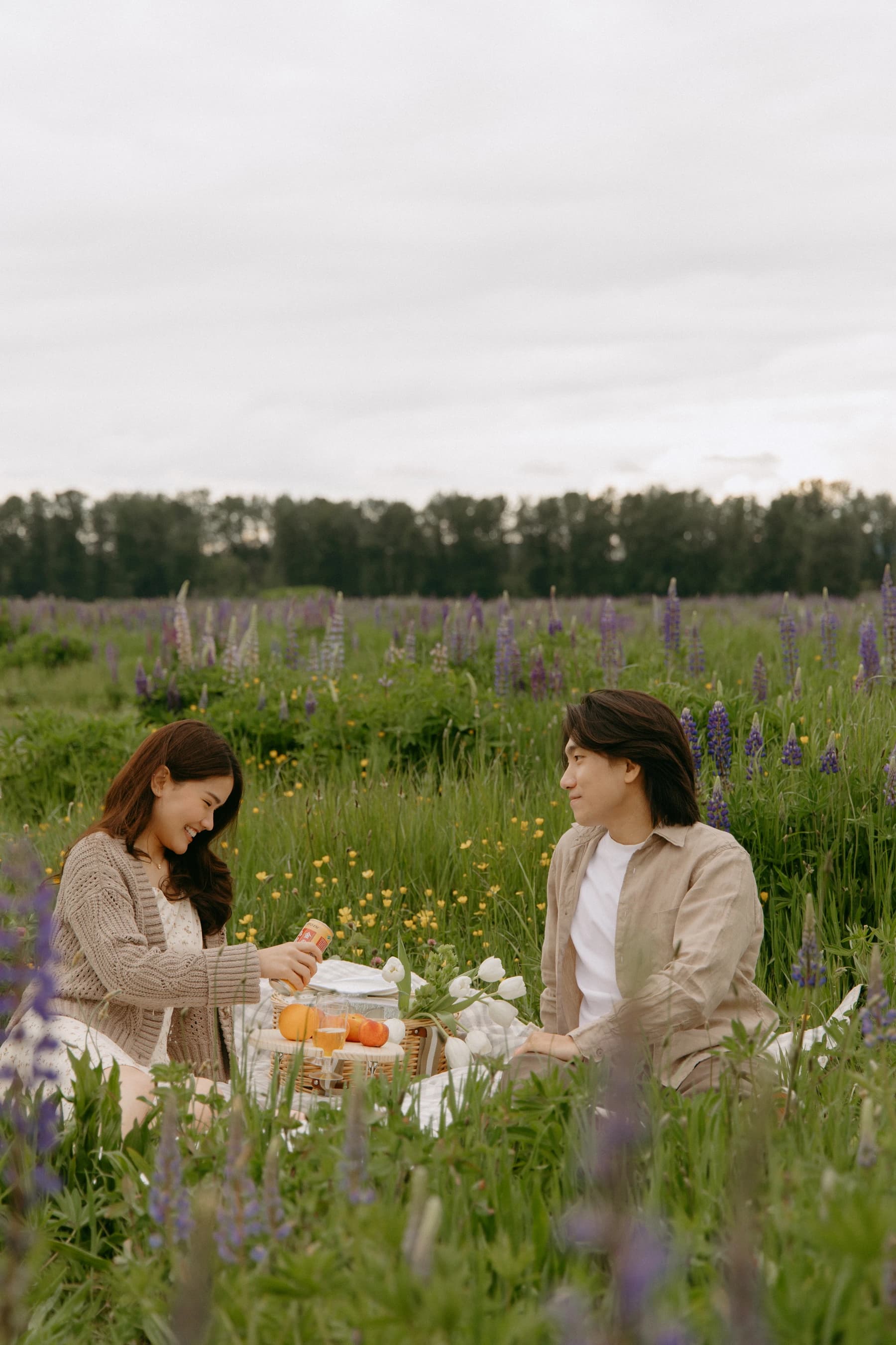 Jam and Tony sitting across a picnic basket in the lupine field, surrounded by peaches and white tulips
