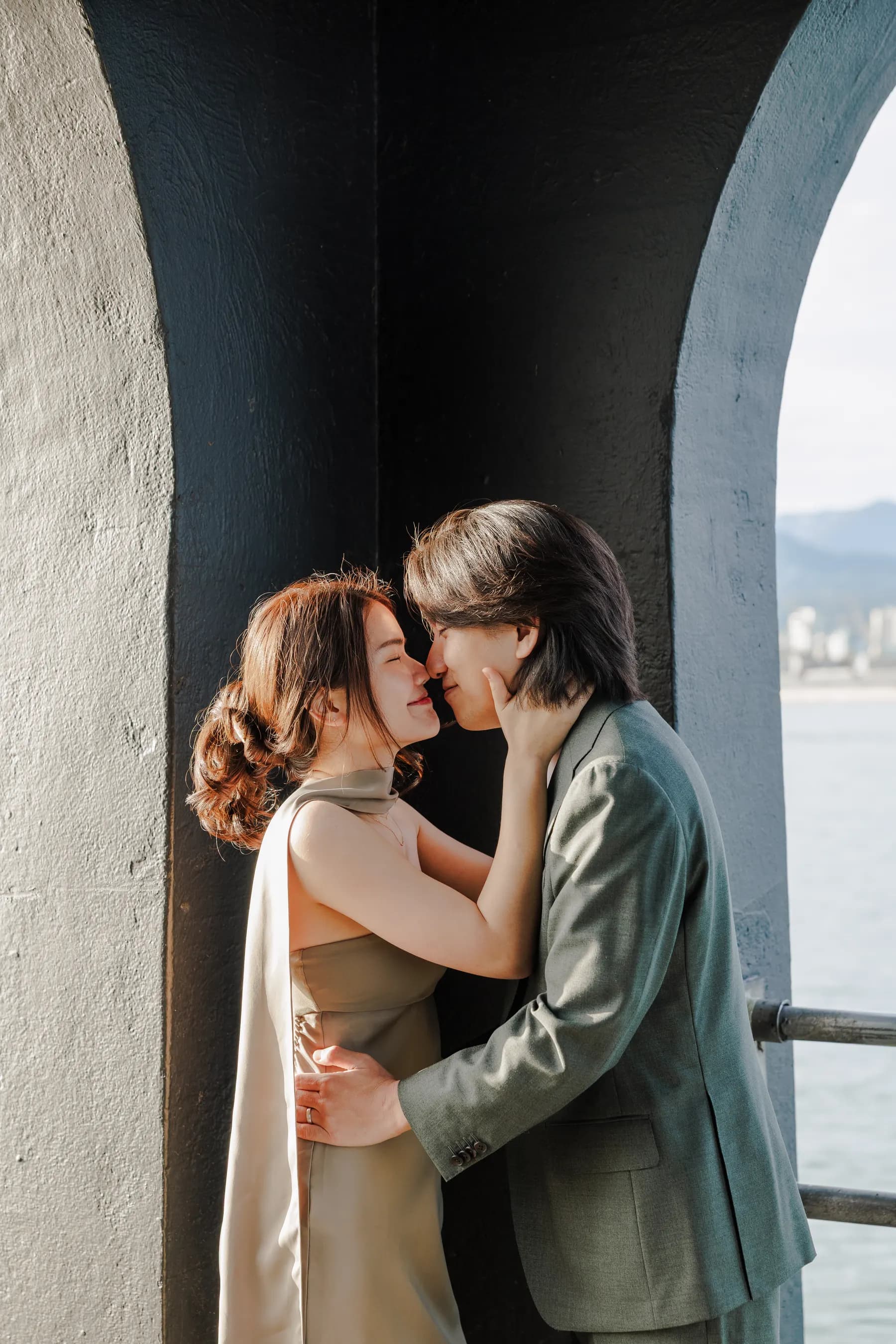 Almost kissing beneath a dark stone archway, mountains and water beyond